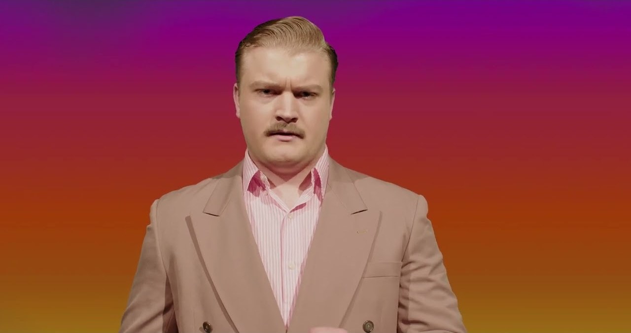 A lawyer in a pale suit addressing camera against a magenta and orange gradient