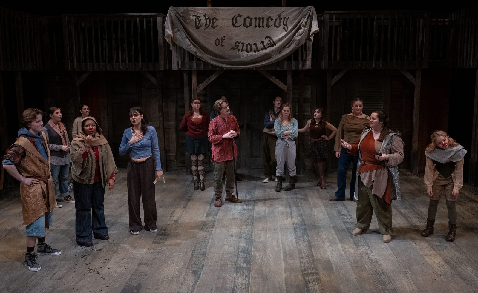 The full company of The Comedy of Errors beneath a hand-painted banner