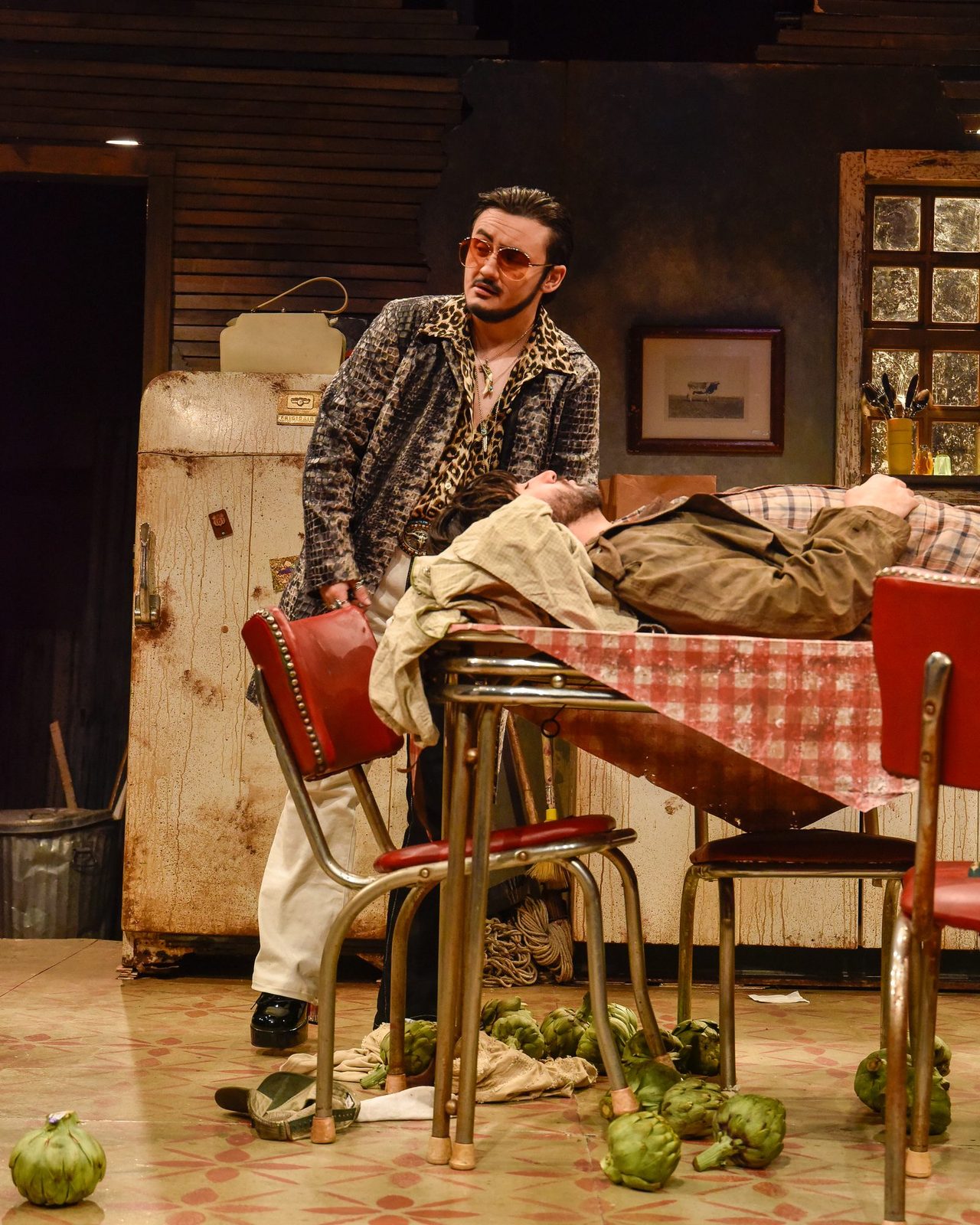 A character among overturned chairs with artichokes strewn across the floor