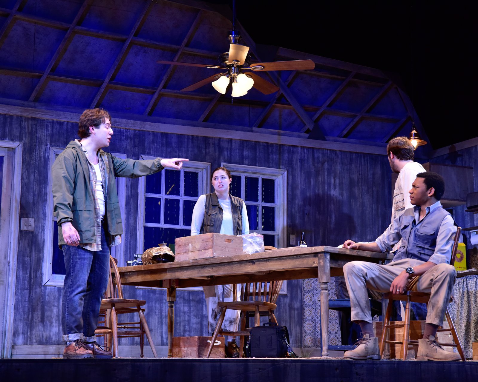 Four characters around the kitchen table at night, blue light through the windows