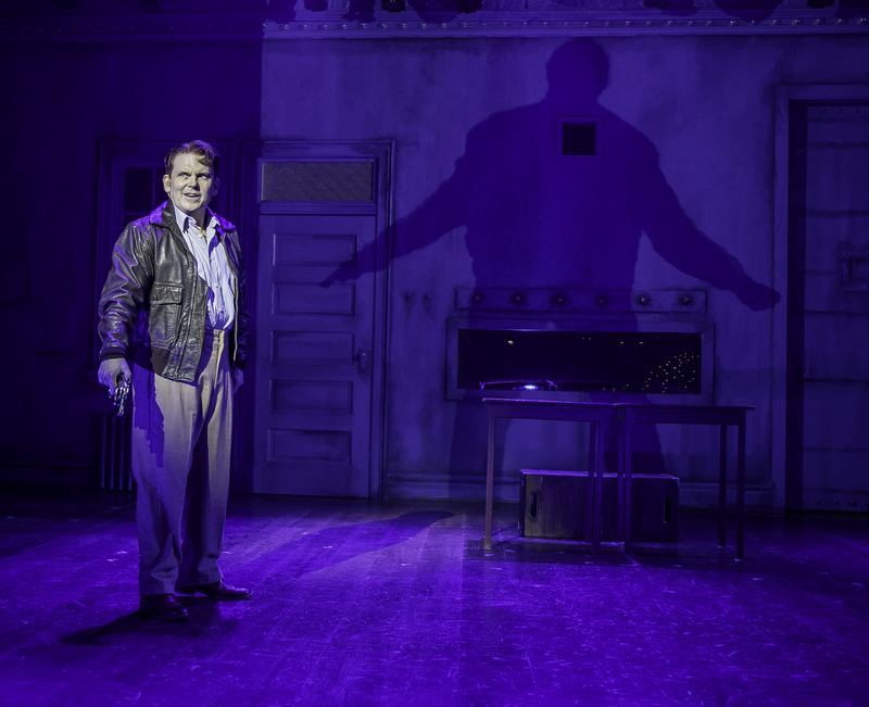 An actor in a hard sidelight throwing a long shadow across a violet wall