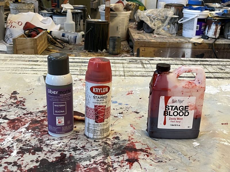 Bottles of stage blood and spray paint on a spattered shop floor