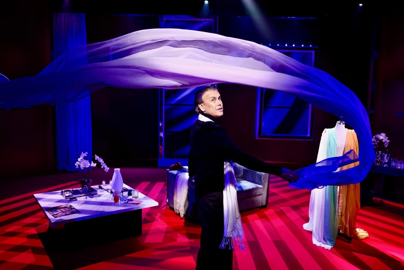Halston sweeping a length of blue chiffon across the studio, a dress form of colored gowns beside him
