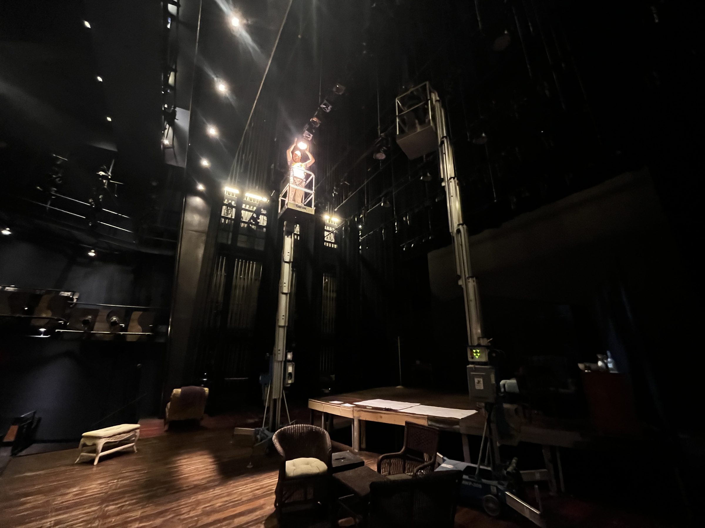 An empty stage during a focus call, booms and a ladder standing in the working light