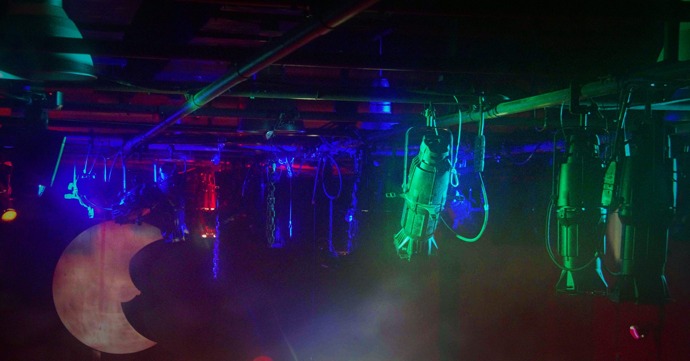 An overhead electric seen from below, fixtures and safeties picked out in blue, red and green, with a crescent moon cut-out hanging at the left
