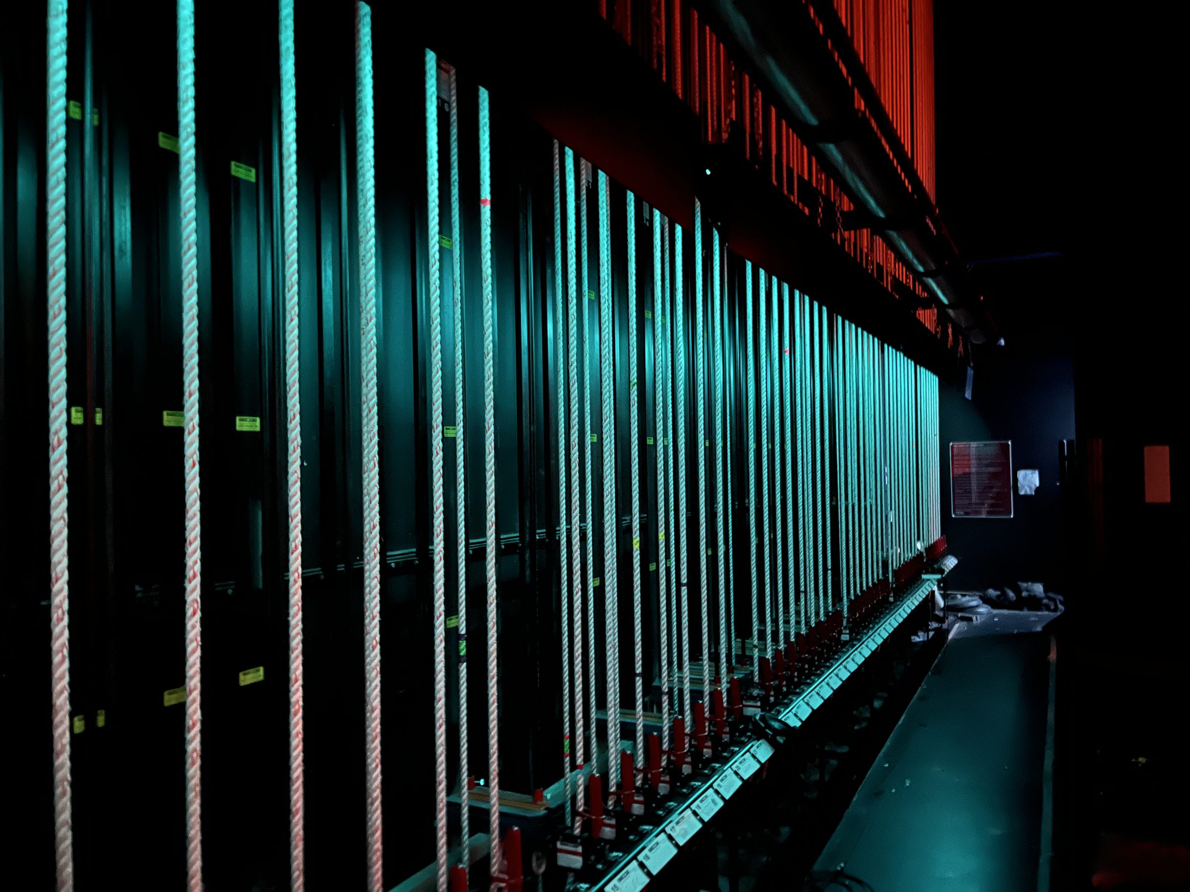 A counterweight fly rail lit in teal, rope lines running floor to grid